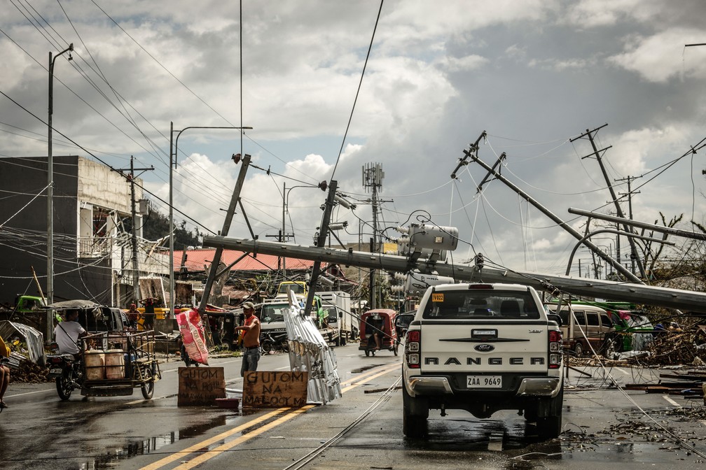 Postes elétricos caídos bloqueiam uma rua na cidade de Surigão, nas Filipinas, neste domingo (19), dias após a passagem do tufão Rai   — Foto: Ferdinandh Cabrera/AFP