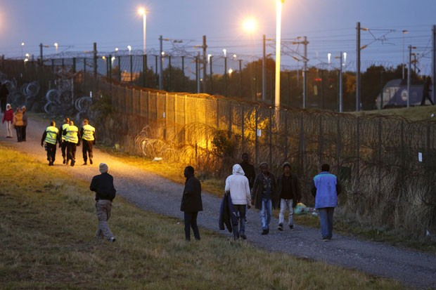 Imigrantes passam por cerca na entrada do túnel do Canal da Mancha em Coquelles, perto de Calais, na França, na noite desta quinta-feira (30) (Foto: Pascal Rossignol/Reuters)