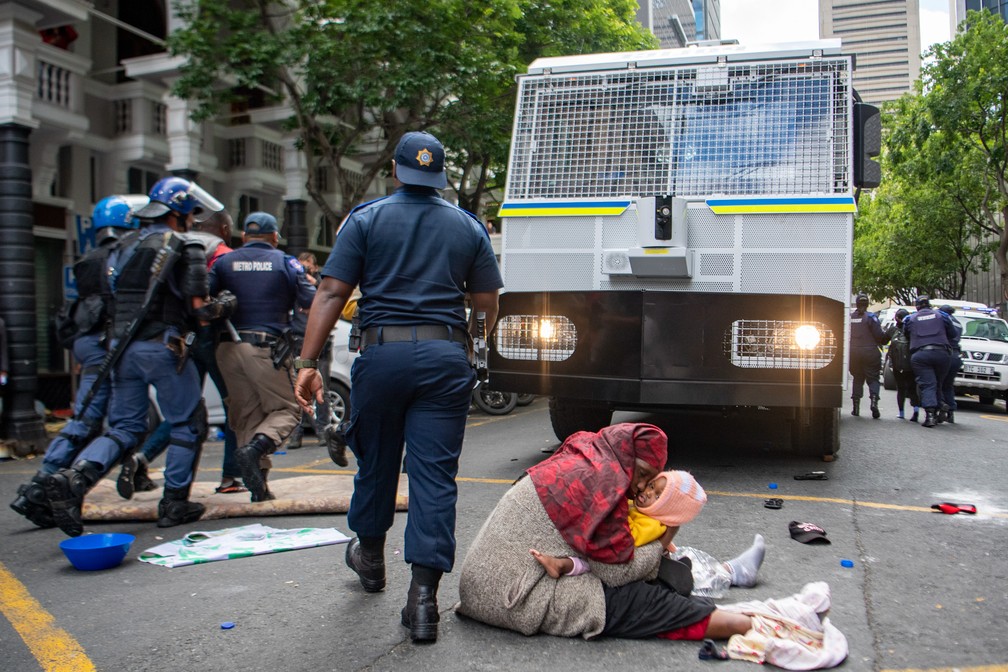 30 de outubro - Uma mulher protege seu bebê durante ação da polícia em protesto do lado de fora do escritório da agência da ONU para refugiados na Cidade do Cabo, na África do Sul. A polícia usou canhões de água enquanto dispersava e prendia dezenas de estrangeiros que acamparam fora dos escritórios por semanas buscando realocação para fora do país após uma onda de ataques a estrangeiros no início deste ano — Foto: Associated Press