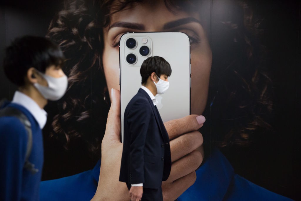 TOKYO, JAPAN - 2020/10/30: Commuters wearing face masks walk past an advertisement for the new iPhone 12 in Tokyo. (Photo by Stanislav Kogiku/SOPA Images/LightRocket via Getty Images) (Foto: SOPA Images/LightRocket via Gett)