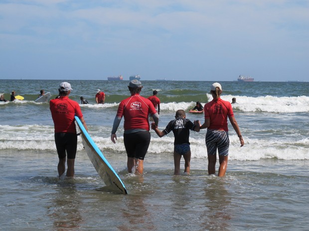 Professores e Rapha entrando no mar para uma aula de surf (Foto: Mariane Rossi/G1)