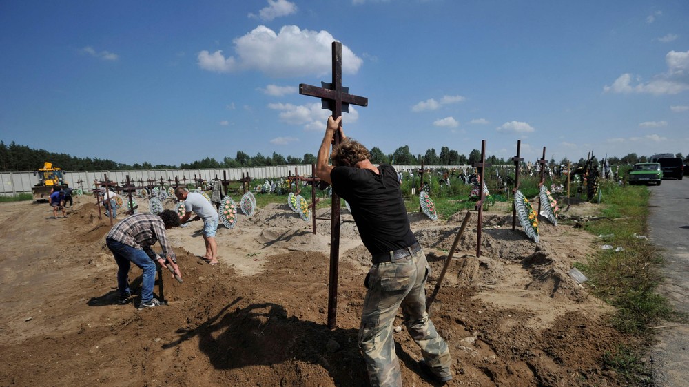 Trabalhadores comunitários enterram caixões durante funeral coletivo de pessoas não identificadas mortas no bimestre fevereiro-março de 2022 no cemitério de Bucha, Ucrânia 