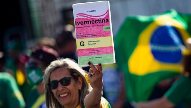 BBC Mulher em manifestação pró-Bolsonaro segura cartaz com desenho de caixa de ivermectina (Foto: Getty Images via BBC)