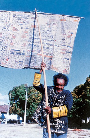 O XERIFE DO HOSPÍCIO  Bispo do Rosário veste um de seus mantos e carrega um estandarte na Colônia Juliano Moreira, na década de 1980. Ele transformou sua cela-forte em ateliê (Foto: divulgação)