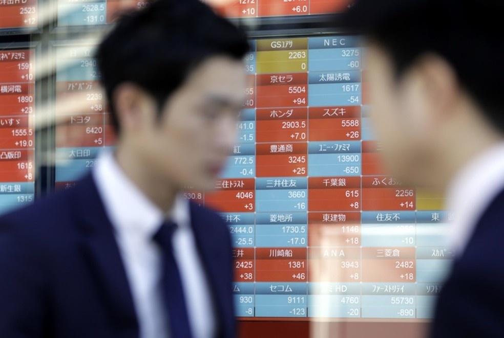 Homens passam em frente a um painel com as cotações das ações na China — Foto: Bloomberg