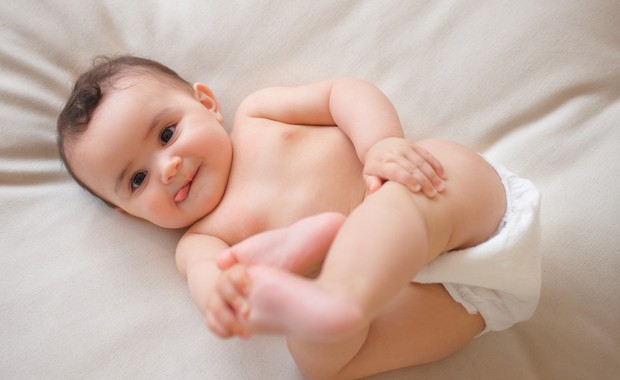 Bebê sorrindo deitado na cama de fralda (Foto: Shutterstock)