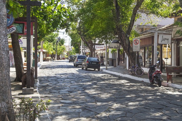 Buzios-RJ, Brazil – September 30, 2011: Famous Rua das Pedras (Stone Street) in Buzios, the main thoroughfare of the city in which are located the sophisticated shops and restaurants. Cars parked along the sidewalk, a bicycle near a tree and a motorcycle  (Foto: Getty Images)