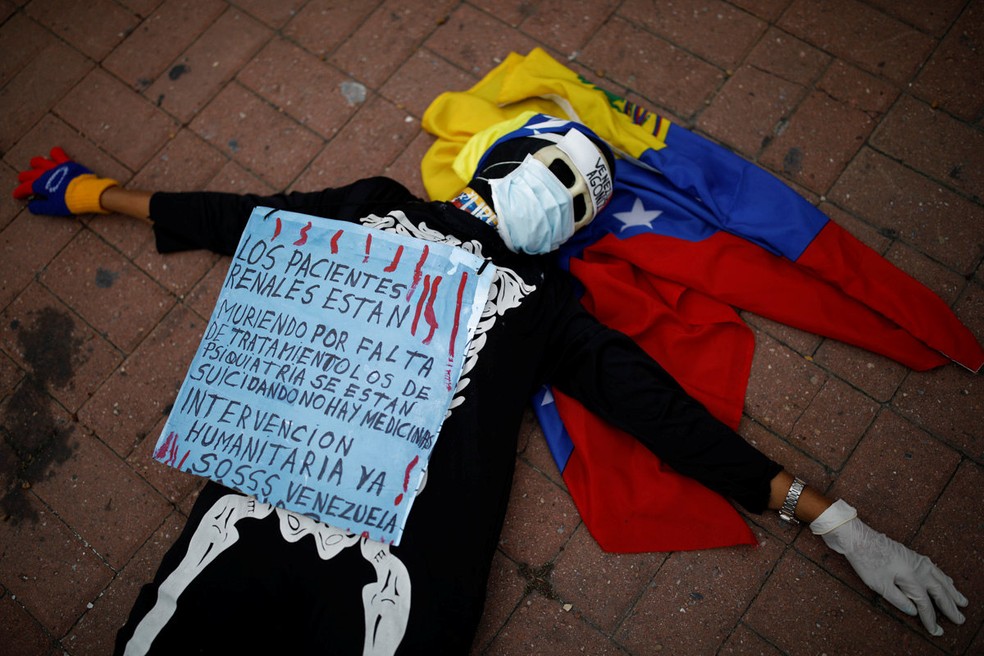 Uma mulher fantasiada de esqueleto participa de um protesto contra a escassez de medicamentos em Caracas, na Venezuela. O cartaz diz: 'Pacientes renais estão morrendo por falta de medicação, pacientes psiquiátricos estão se suicidando. Não há medicamentos. Intervenção humanitária, já. SOS Venezuela' (Foto: Carlos Garcia Rawlins/Reuters)