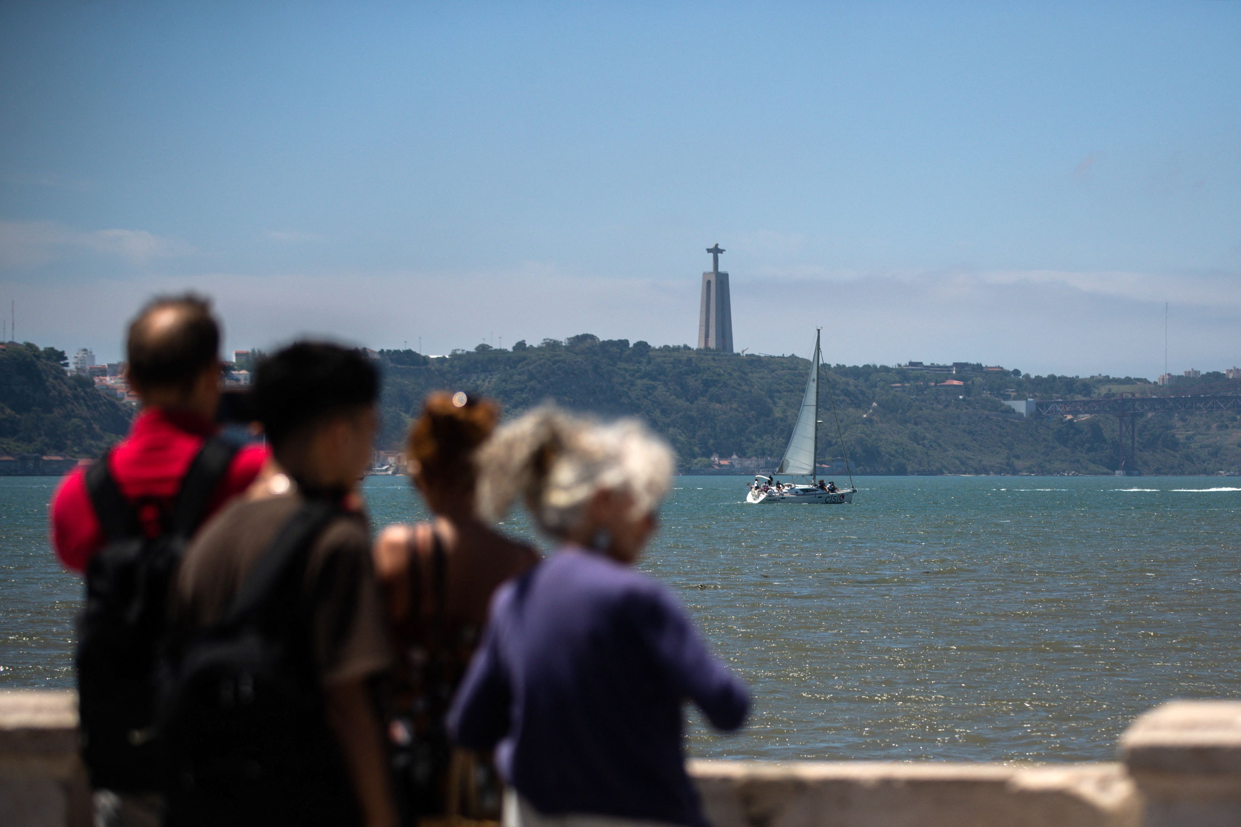 Em Lisboa: turistas à beira do Tejo observam o Cristo Rei