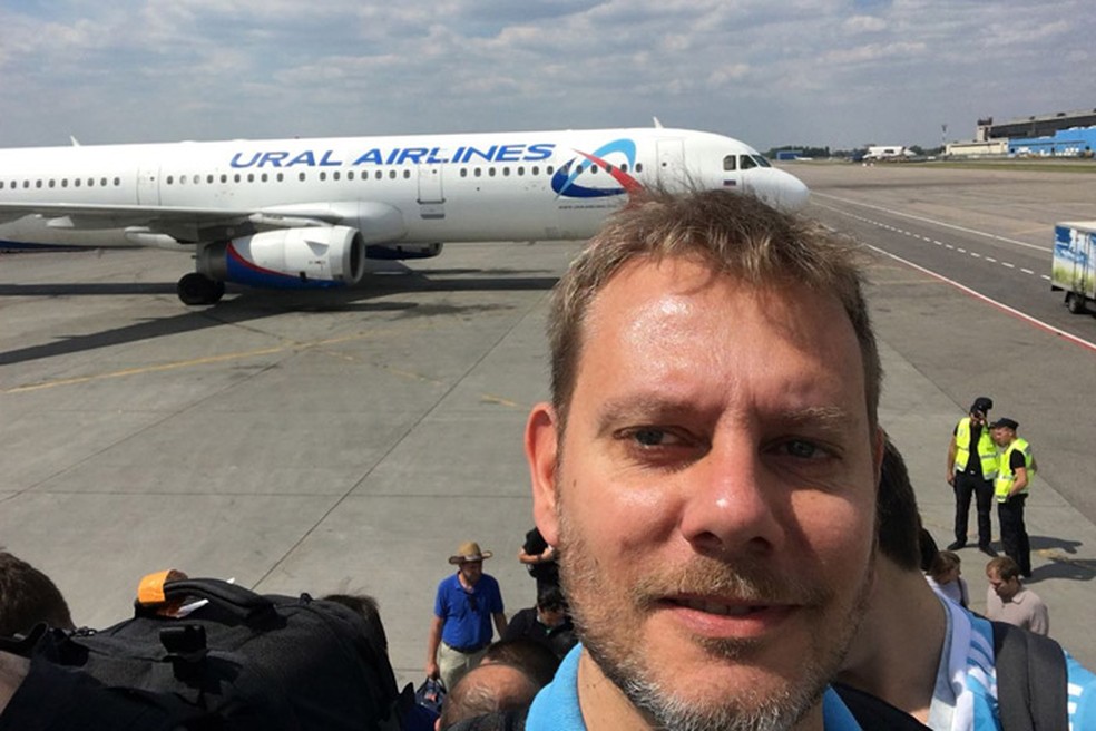 O jornalista argentino Sebastian Fest tira selfie com um avião da Ural Airlines ao fundo, em um aeroporto russo (Foto: Arquivo pessoal/Sebastian Fest)