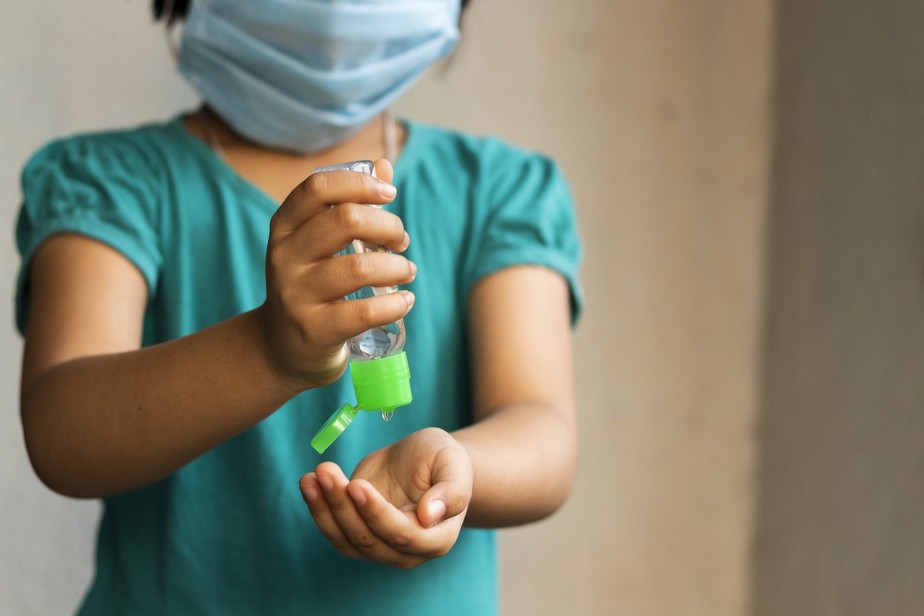 Criança usando máscara contra covid-19 passa álcool em gel na mão
