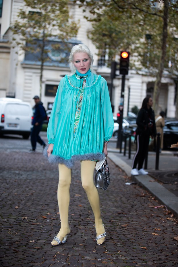 PARIS, FRANCE - OCTOBER 2: Lotta Volkova wears a teal baby doll dress, silver Miu Miu purse, yellow leggings, and silver transparent heels before the Miu Miu show during Paris Fashion Week Spring/Summer 2019 on October 2, 2018 in Paris, France. (Photo by  (Foto: Getty Images)