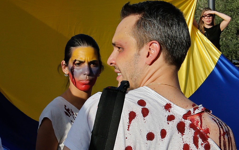 Manifestantes exibem sangue falso durante protesto contra a Constituinte venezuelana em Madri, na Espanha, no domingo (30) (Foto: AP Photo/Paul White)