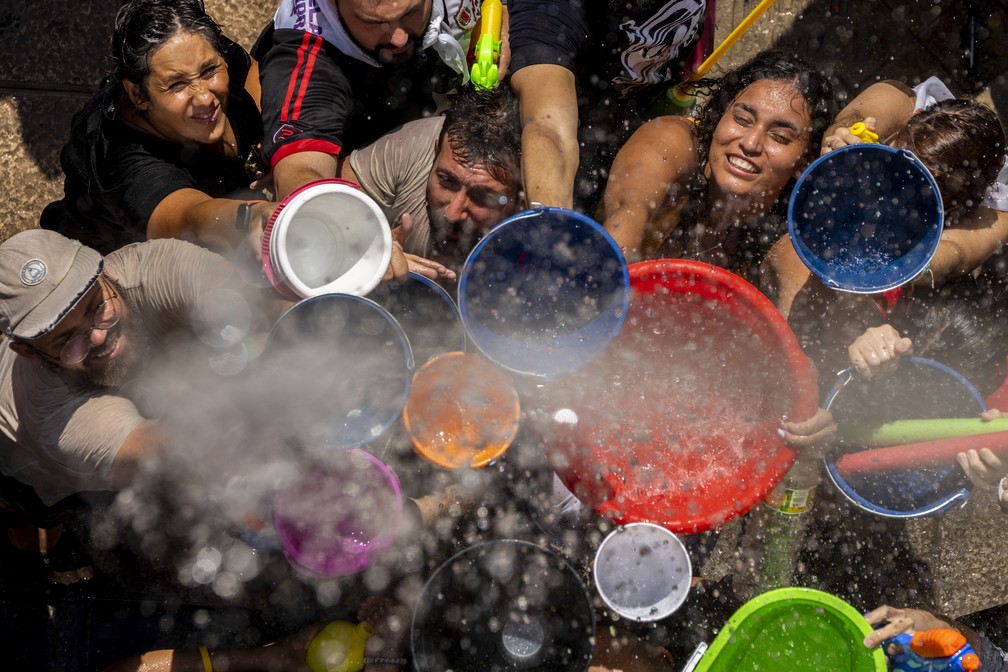Pessoas enchem seus baldes e tigelas em uma 'batalha de águas' típica do festival de Vallecas, na Espanha. — Foto: AP Photo/Manu Fernandez