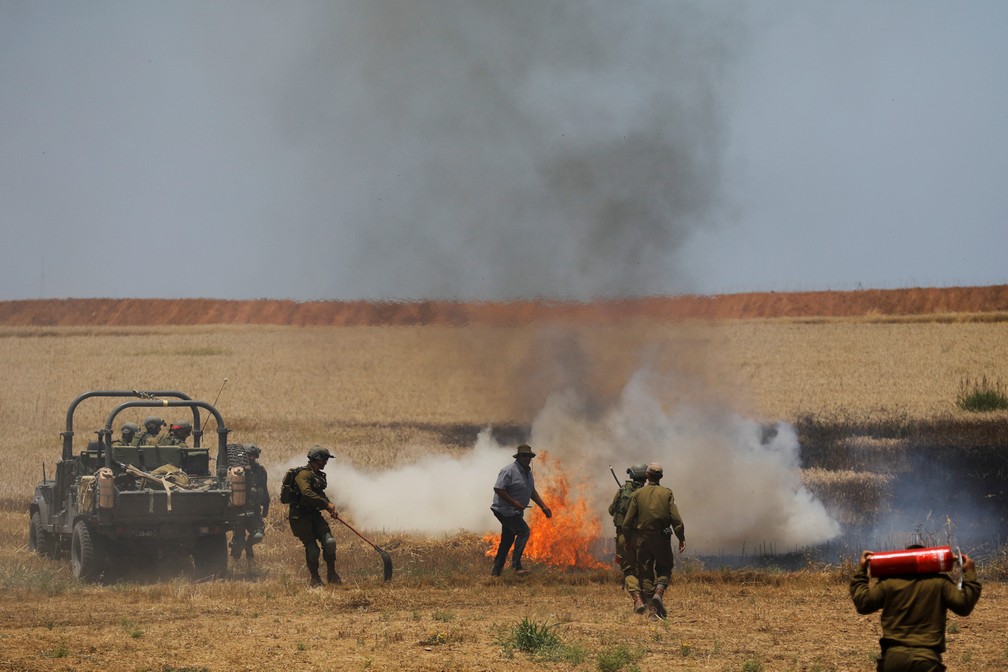 Soldados israelenses tentam apagar um incÃªndio em um campo do lado israelense da fronteira com Gaza nesta segunda (Foto: Amir Cohen/Reuters)