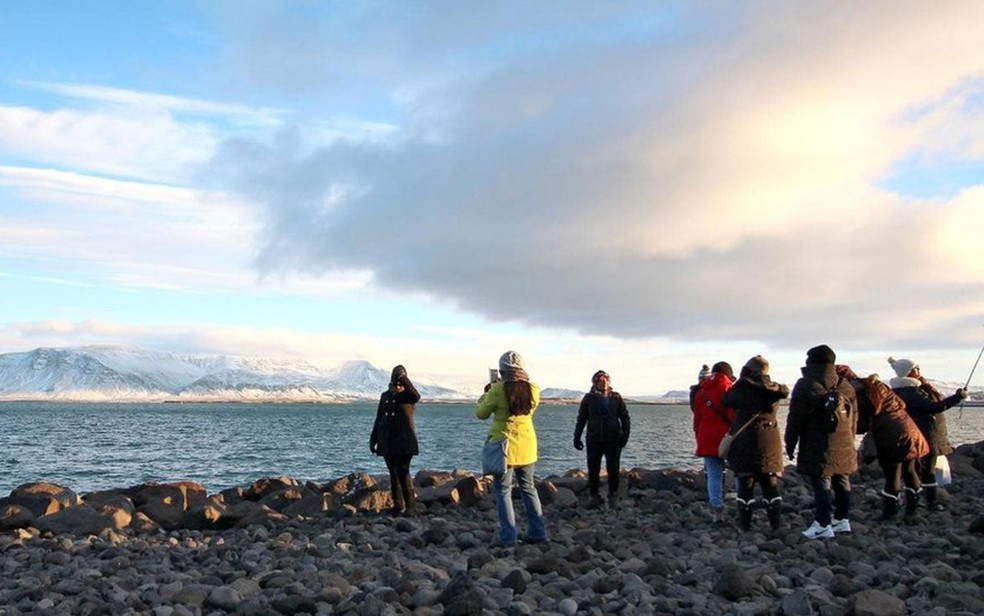 Turistas posam diante de geleira em Reykjavík Image caption Um número de turistas várias vezes maior que a população islandesa visitou o país em 2016  (Foto: Chris Baraniuk/BBC)