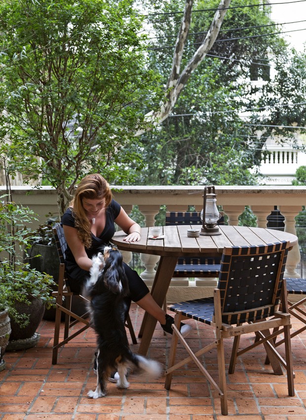 VARANDA | A arquiteta e moradora Ana Angrimani com seu pet Brunello. Mesa Timbó e cadeiras Maresias, ambas de Carlos Motta.  (Foto: Julia Ribeiro/Divulgação)