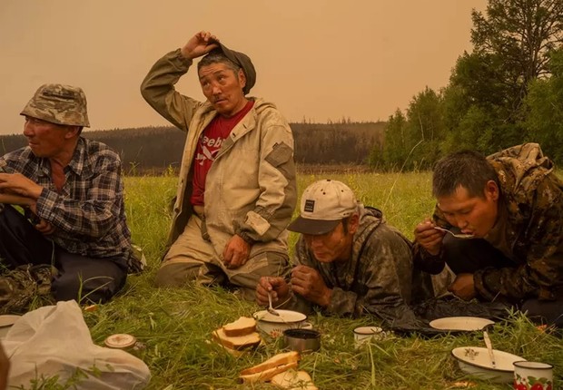 Voluntários locais de combate a incêndios fazem uma pausa para comer em um campo em Magaras, Sakha central, Sibéria, Rússia, em 1º de julho de 2021 (Foto: NANNA HEITMANN PARA MAGNUM PHOTOS via BBC)