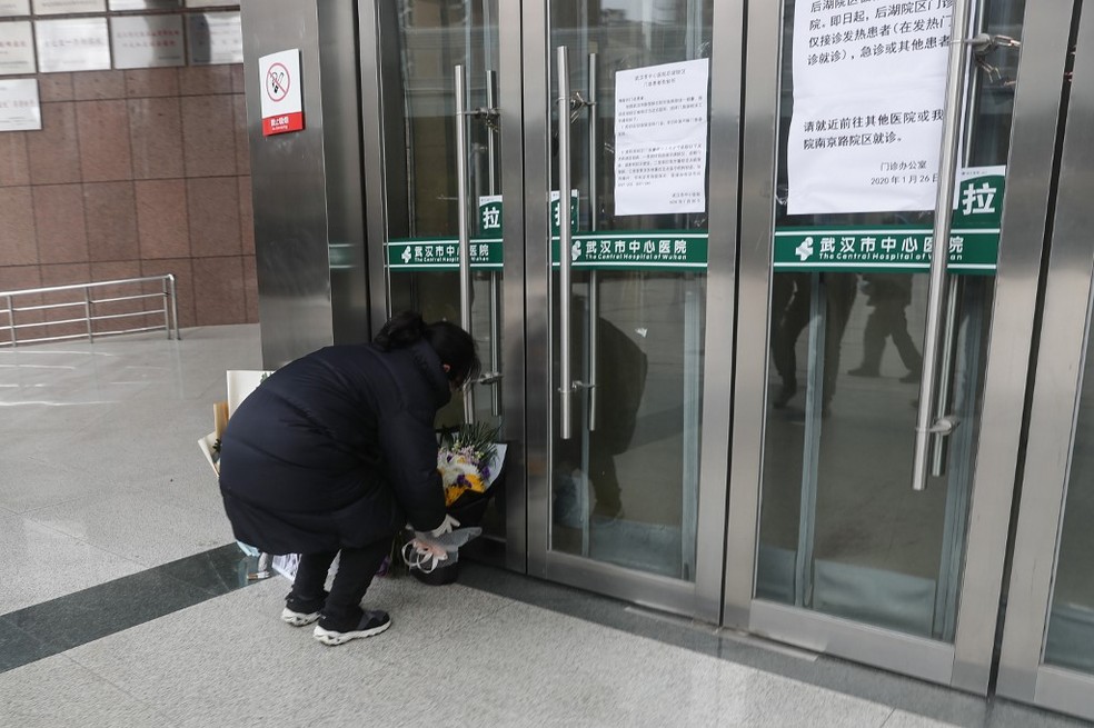 Mulher é vista colocando flores em frente ao Hospital Central de Wuhan, onde o médico oftalmologista Li Wenliang morreu com coronavírus; ele chegou a ser investigado pela polícia por 'espalhar boatos' quando identificou o coronavírus antes da doença se tornar um surto internacional. — Foto: STR/AFP