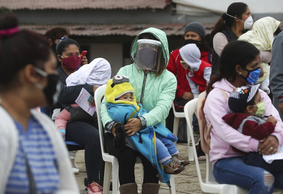 Mulheres com máscaras seguram crianças em Lima, Peru, em imagem de junho — Foto: AP Photo/Martin Mejia