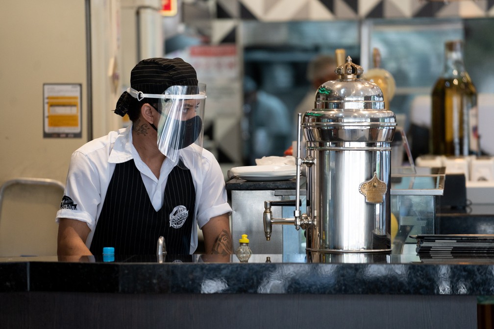 Funcionário de restaurante na Zona Sul, em São Paulo, usa máscara e protetor facial na reabertura para o público — Foto: Marcelo Brandt/G1