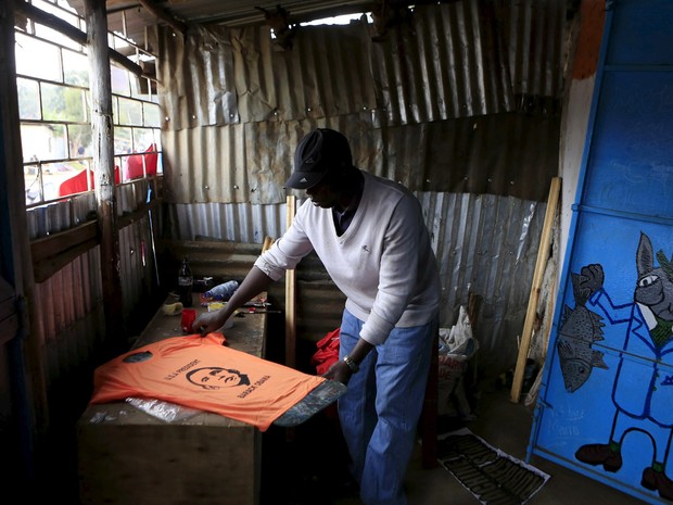 Wycliff Madegwa pega uma camiseta exibindo a imagem do presidente dos EUA Barack Obama em sua oficina na favela de Kibera em Nairobi, no Quênia. Obama, de origem queniana, visita o país com a missão de fortalecer os laços econômicos e a segurança dos EUA (Foto: Noor Khamis/Reuters)