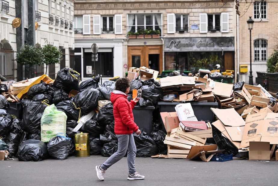 Um pedestre passa por contêineres de lixo doméstico em uma rua de Paris