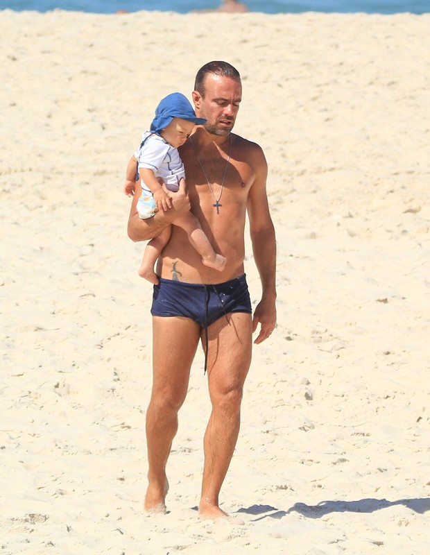 Roger Flores com o filho, Tom, no colo em dia de praia (Foto: Fabricio Pioyani/ Agnews)