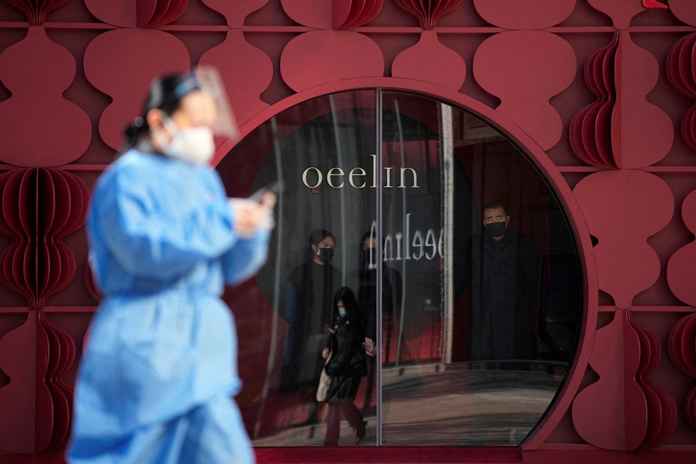 Uma mulher em um traje de proteção passa por uma loja, enquanto os surtos da doença da Covid-19 continuam, em Xangai, na China — Foto: REUTERS/Aly Song 