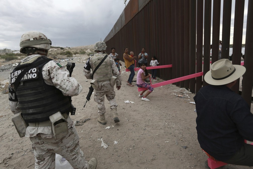 28 de julho - Militares mexicanos observam enquanto pessoas brincam em gangorras instaladas no muro que separa os Estados Unidos do México. O brinquedo fica em um trecho da fronteira entre El Paso (EUA) e Ciudad Juaréz (México) e foi uma maneira de unir, de uma forma 'lúdica', os dois países, segundo os idealizadores do projeto — Foto: Christian Chavez/AP