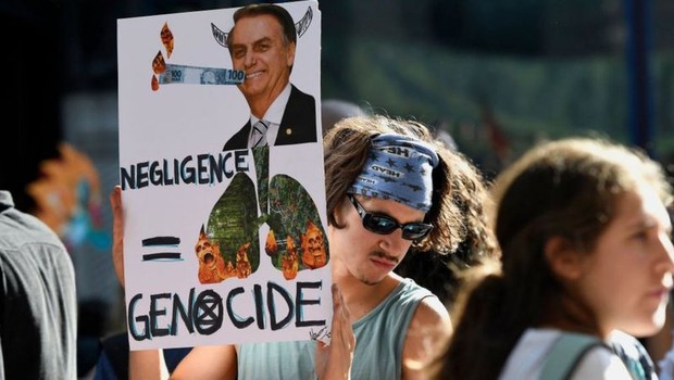 BBC Em Londres, ativista segura cartaz com foto de Bolsonaro e de florestas em chamas, com as palavras 'negligência' e 'genocídio' em inglês (Foto: Getty Images via BBC)