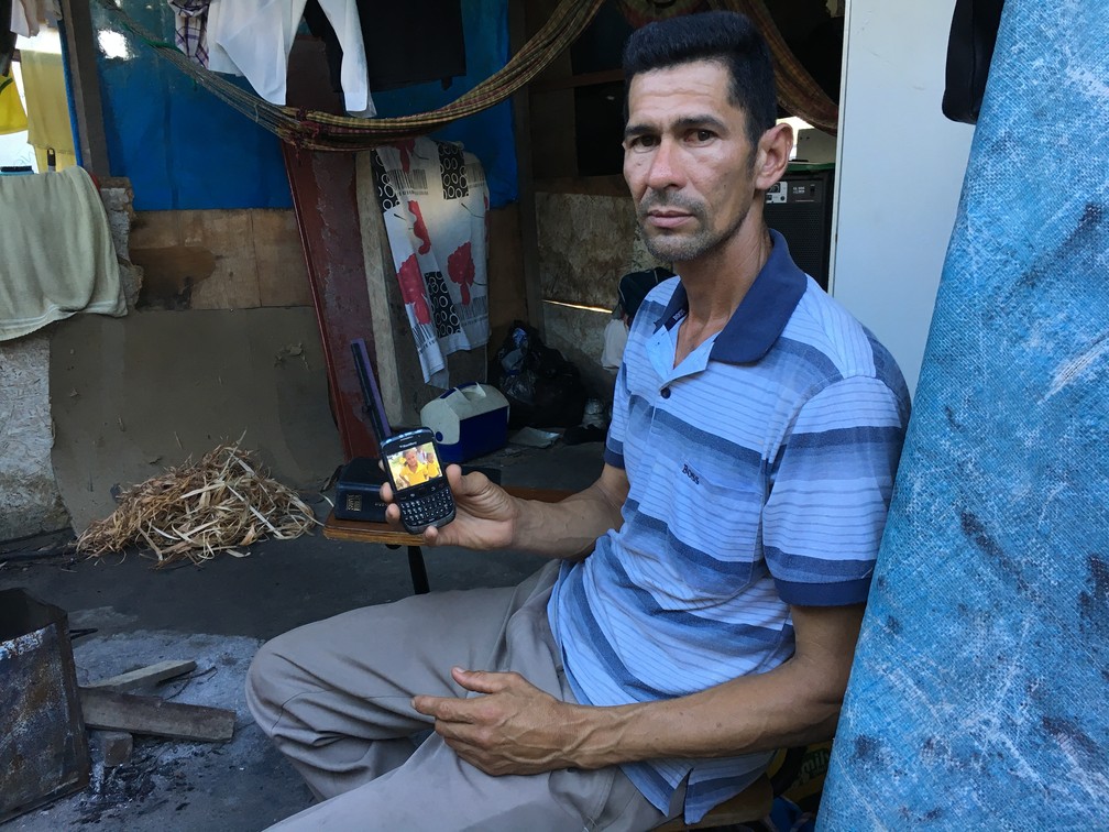 Reinaldo Rondon, 43 anos, mostra foto dos filhos no telefone; aparelho não faz chamadas e há semanas ele não fala com a família que continua na Venezuela — Foto: Emily Costa/G1 RR