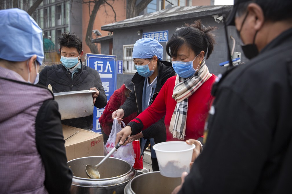 Trabalhadores com máscaras contra o novo coronavírus entregam almoço em Pequim, na China, nesta sexta-feira (21). — Foto: Mark Schiefelbein/AP