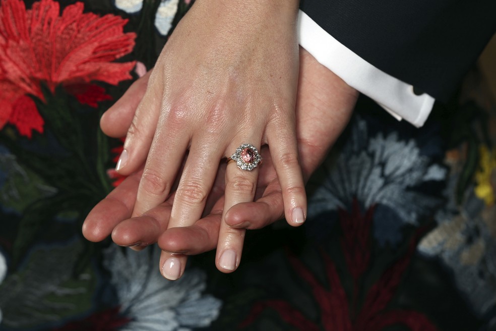 A princesa britânica Eugenie exibe seu anel de noivado, com uma safira rodeada por diamantes, ao posar com o noivo Jack Brooksbank no Palácio de Buckingham, na segunda-feira (22) (Foto: Jonathan Brady/Pool Photo via AP)