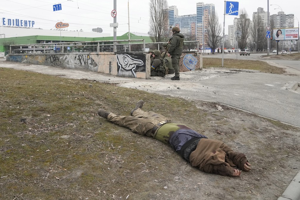 25 de fevereiro - Corpo de um soldado é visto enquanto soldados do Exército ucraniano se sentam ao lado, em Kiev, Ucrânia — Foto: Efrem Lukatsky/AP
