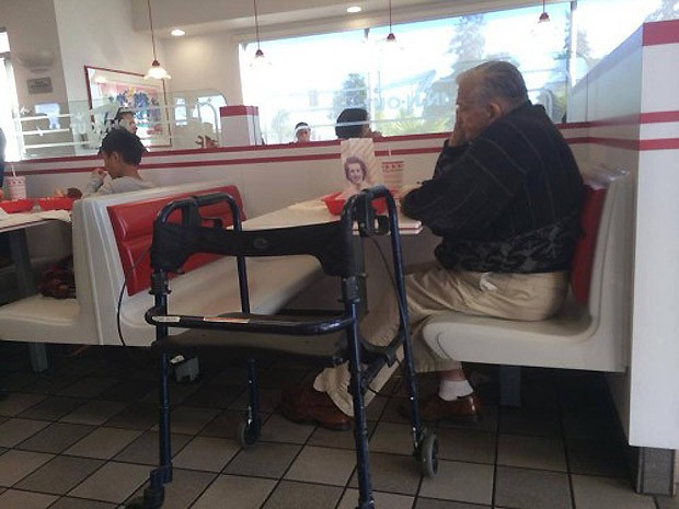 O senhor de cabelos brancos sentado à mesa com a foto que seria de sua esposa, com quem viveu 55 anos (Foto: Reprodução / Imgur)
