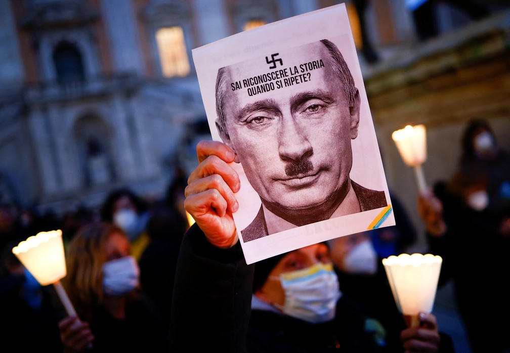 25/02/2022 - Manifestantes em Roma exibem cartaz com a imagem de Vladimir Putin com um bigode de Adolf Hitler e uma suástica, símbolo nazista — Foto: Guglielmo Mangiapane/Reuters