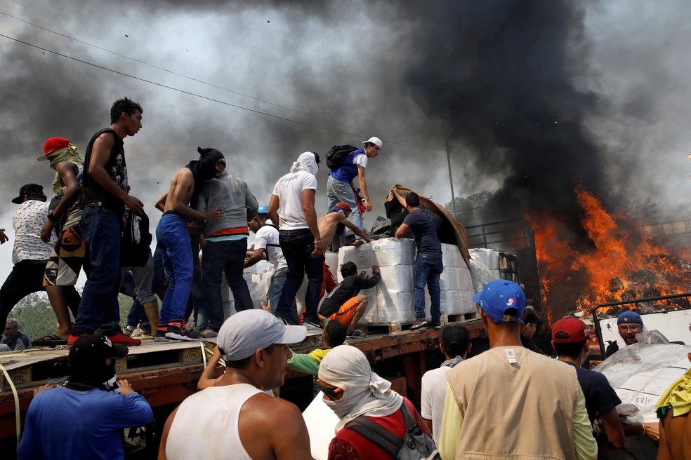 Após confrontos com as forças de segurança da Venezuela, manifestantes tentam recuperar a carga do caminhão incendiado — Foto: Marco Bello/Reuters