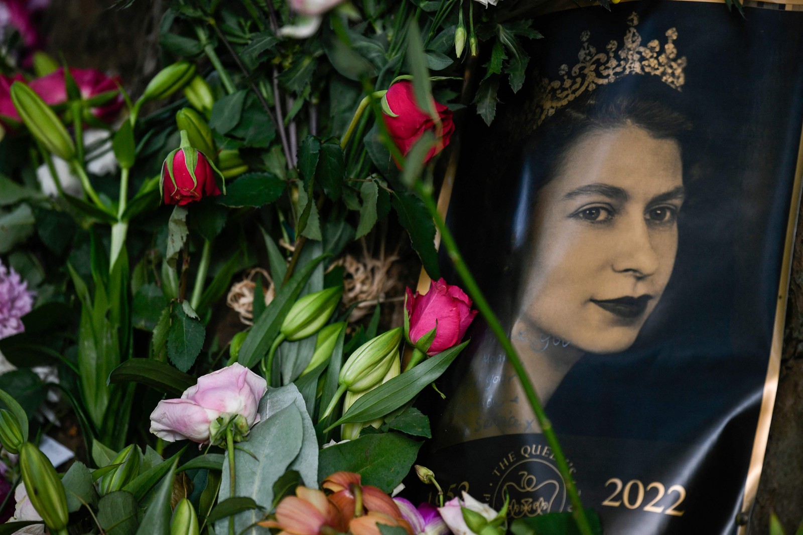Retrato da Rainha Elizabeth II é visto ao lado de flores colocadas do lado de fora do Palácio de Buckingham, em Londres. — Foto: STEPHANE DE SAKUTIN / AFP