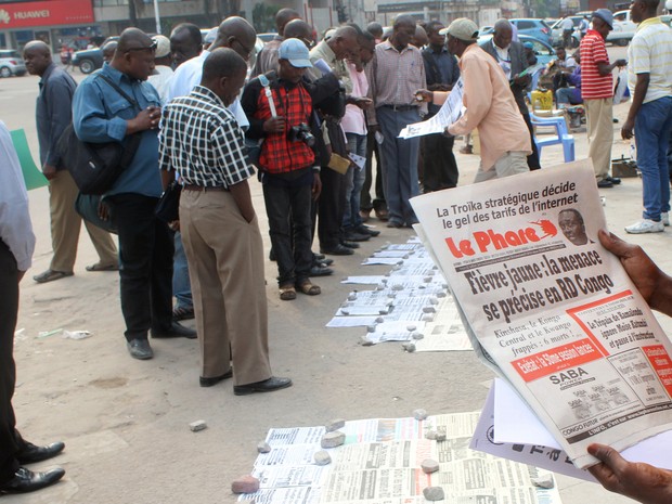  Moradores lêem jornais com notícias sobre o surto de febre amarela nas ruas de Kinshasa, capital da República Democrática do Congo, nesta terça-feira (21)  (Foto: Reuters/Jean Robert N&#39;Kengo)