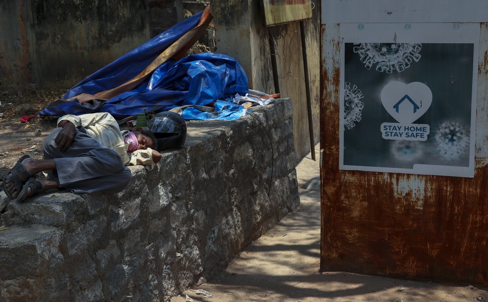 Pessoa dorme ao lado de placa pedindo às pessoas que fiquem em casa para se proteger da Covid-19 em um hospital em Hyderabad, na Índia, em 29 de abril de 2021 — Foto: Mahesh Kumar A./AP