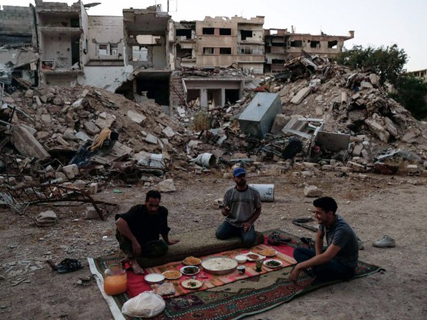 Combatentes do Exército Sírio pela Libertação fazem refeição em frente a prédios destruído na quinta-feira (16)  (Foto: Sameer Al-Doumy / AFP)