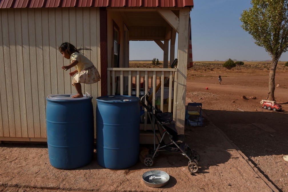 Ravynn Weeks, de 2 anos, pula em contêineres de água na frente de sua casa na Bodaway Chapter — Foto: Stephanie Keith/Reuters