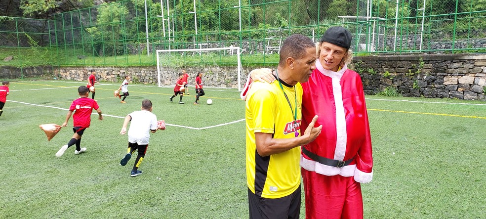 David Luiz abra&ccedil;a Marquinhos, respons&aacute;vel pela Escola Flamengo Social Mangueira, enquanto a crian&ccedil;ada, com presentes na m&atilde;o, corre atr&aacute;s da bola &mdash; Foto: Fred Gomes