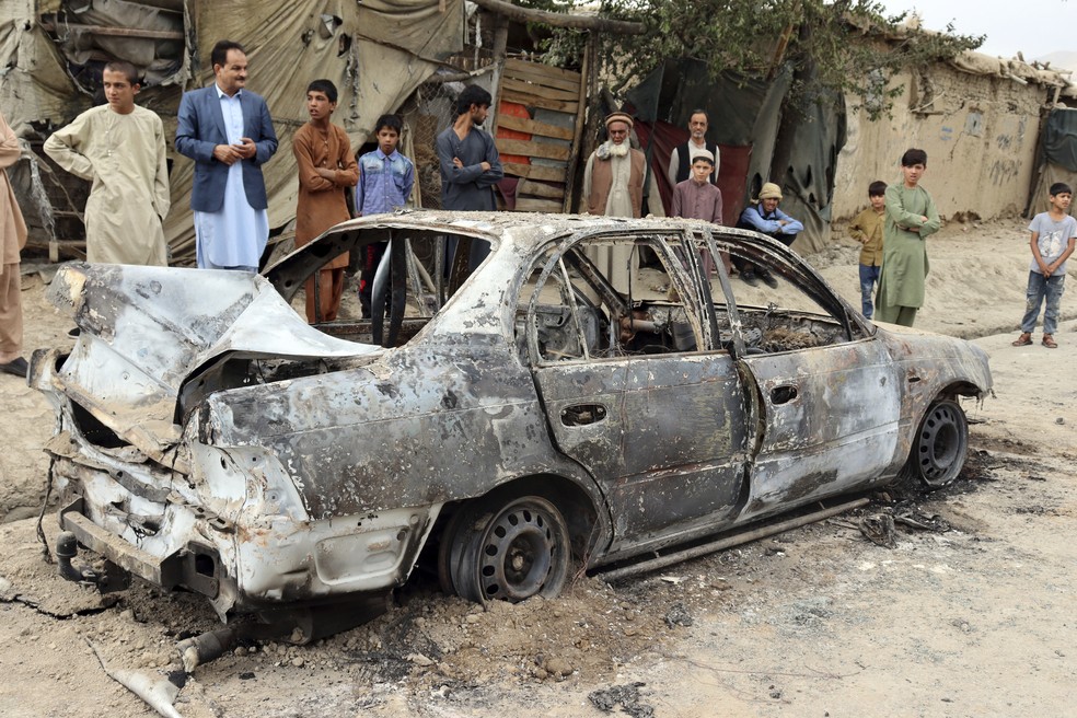 Moradores olham para veículo danificado por um ataque de foguete em Cabul, capital do Afeganistão, em 30 de agosto de 2021. Foguetes atingiram um bairro próximo ao aeroporto internacional Hamid Karzai. — Foto: Khwaja Tawfiq Sediqi/AP