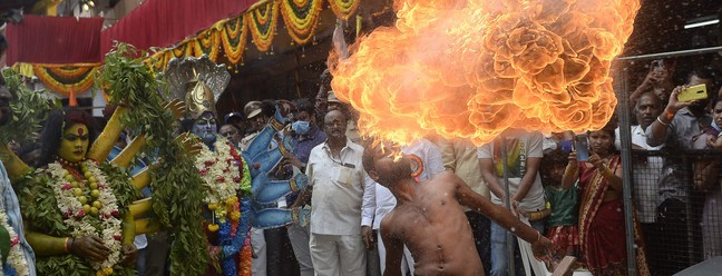 Artistas vestidos como deusas hindus se apresentam ao lado de um homem que cospe fogo durante a procissão do festival Bonalu, no Templo Sri Ujjaini Mahakali, em Secunderabad, a cidade gêmea de Hyderabad, na Índia — Foto: NOAH SEELAM / AFP