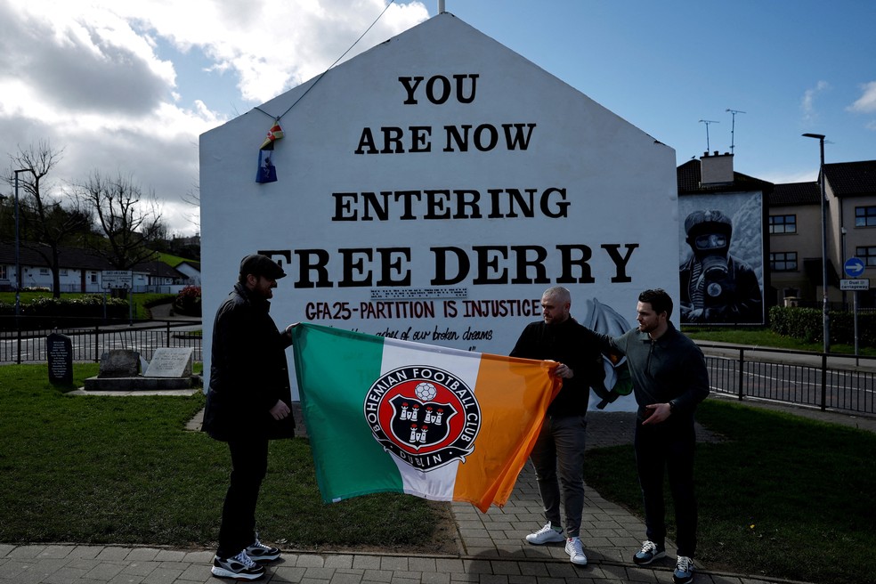 Pessoas seguram uma bandeira com as cores da Irlanda na frente do Free Derry Corner, em 10 de abril de 2023 — Foto: Clodagh Kilcoyne/REUTERS