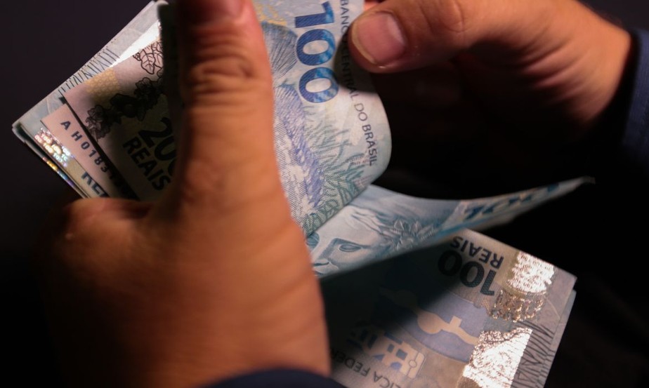 Notas de R$ 100 nas mãos de um trabalhador