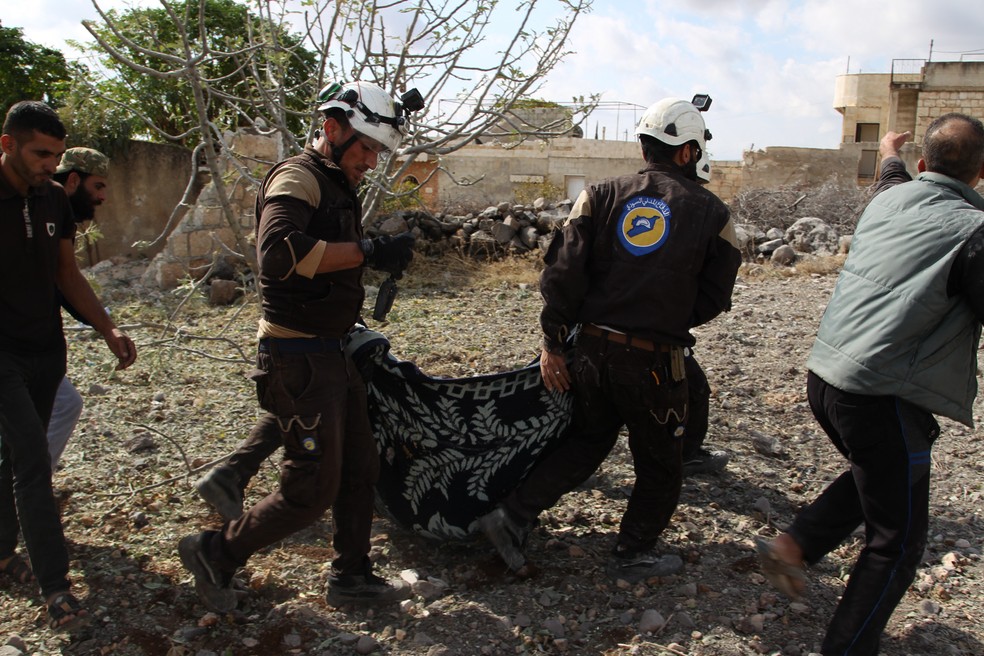 Membros da Defesa Civil da Síria carregam os corpos das vítimas de um ataque aéreo russo na vila de Jaballa, sul de Idlib, neste sábado (02) — Foto: Abdulazez Ketaz/AFP