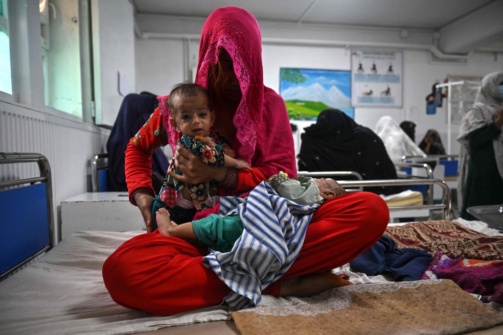 Uma mãe senta em uma cama de hospital com os gêmeos de quatro meses na ala de atendimento à desnutrição no hospital do MSF em Lashkar Gah, Afeganistão — Foto: Lillian Suwanrumpha / AFP